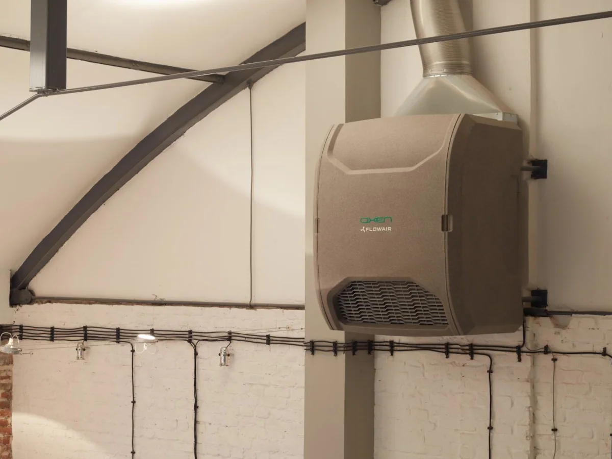 Rekuperator ścienny z nagrzewnicą elektryczną Flowair Oxen zamontowany na ścianie – obudowa z EPP z kratką nawiewną i przyłączem czerpni